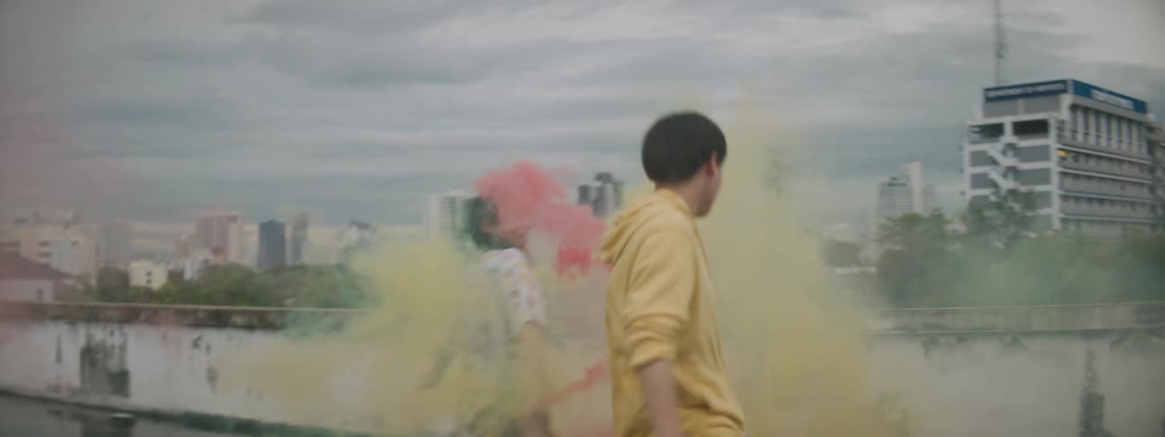 Man and woman dance wet building roof spreading colored smoke with skyline in background