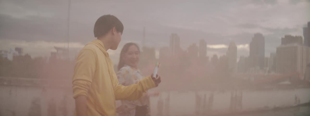 Twopeople dance in colored smoke with city skyline in background
