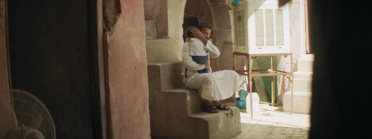 Father holds child close while sitting on steps in courtyard