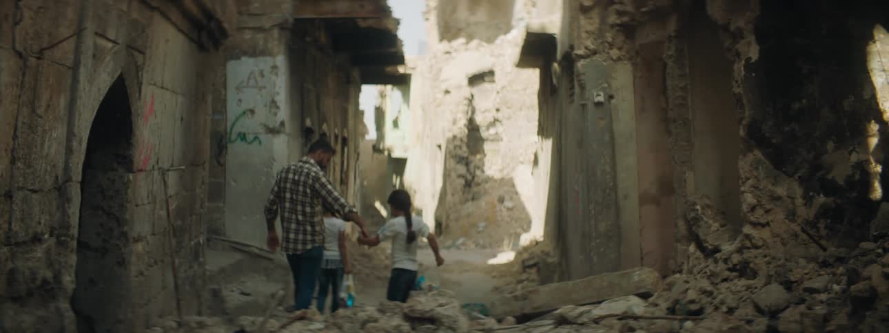 A man helps his children walk through an alley filled with rubble