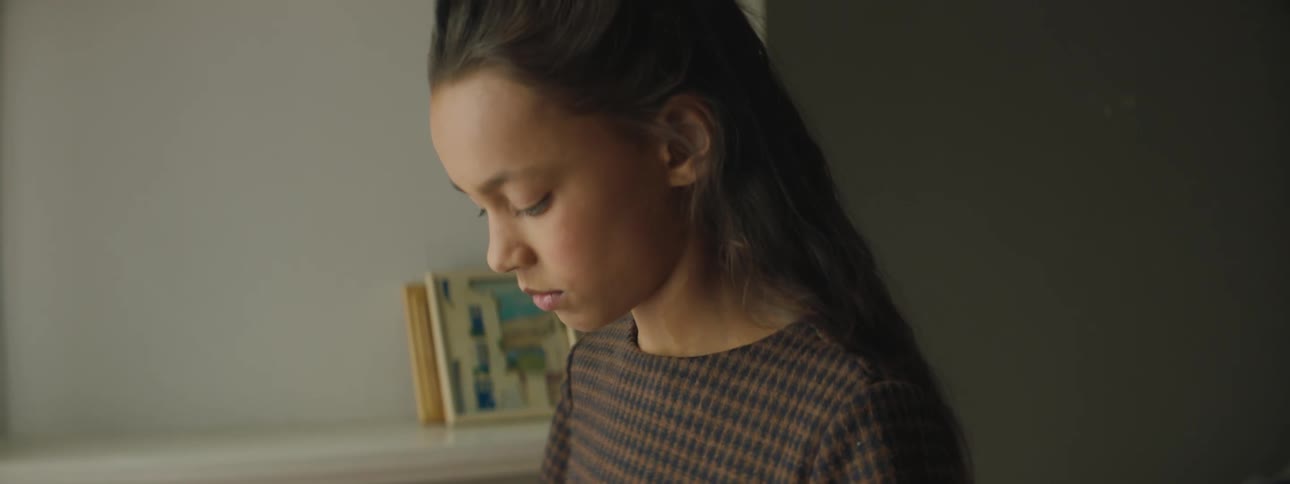 A girl cleans a photograph on her dress before gazing it and looking upwards lost in thought