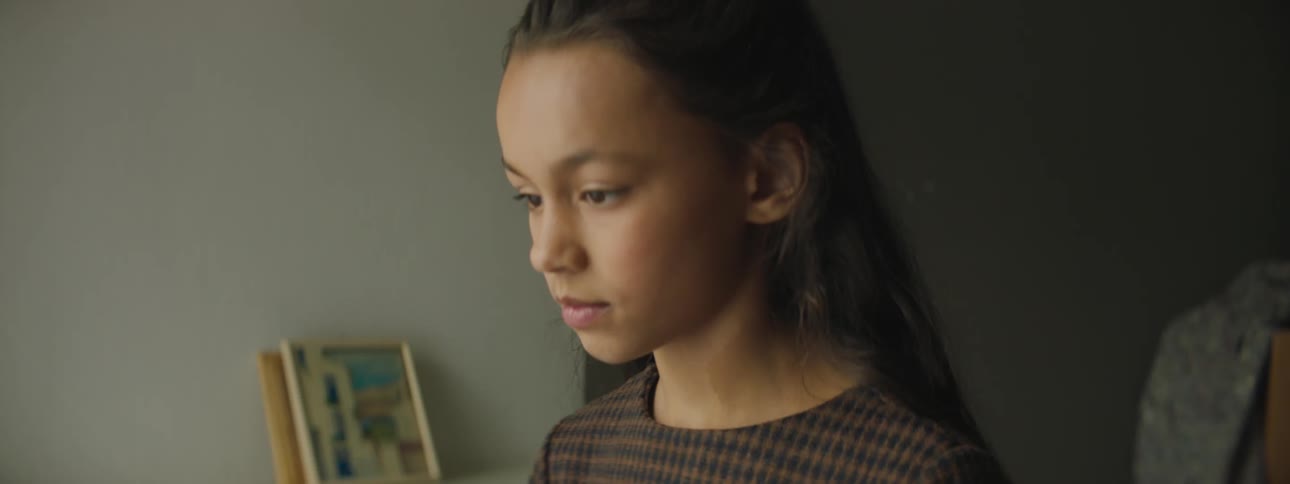 A young girl standing by the mantle in her home