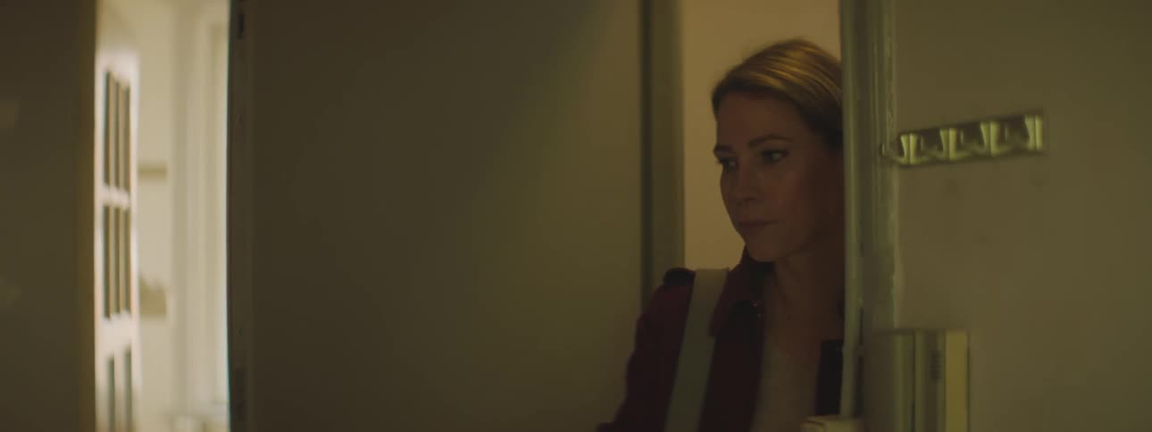 A woman stands with a door open while she waits for a child to run in and then she hangs keys up and closes the door