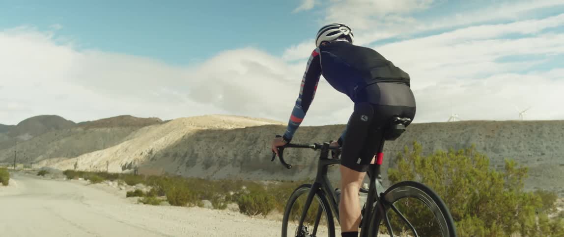 A man wearing a bicycle helmet is riding a bike on a road near mountains