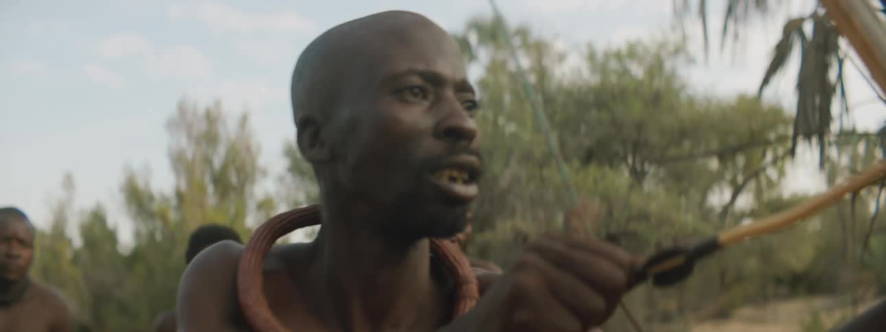A man in a tribe aims a bow and arrow