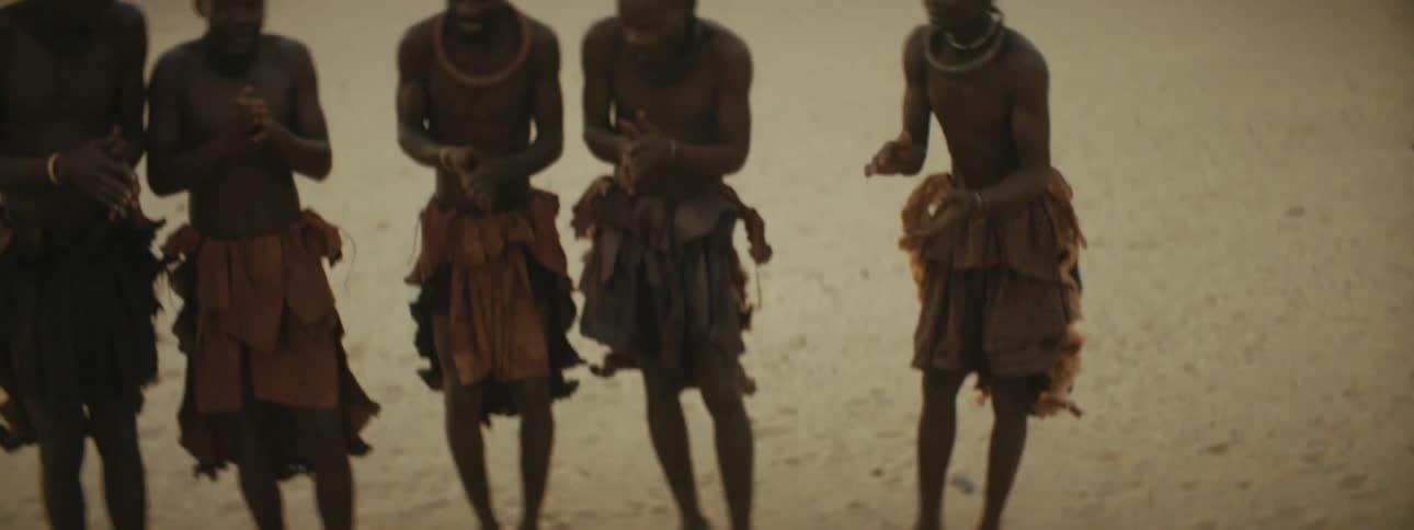Five tribesmen standing in a line and clapping together in the middle of a mountainous desert