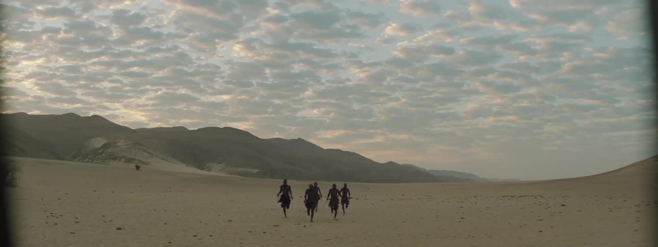 Men run from mist covered mountain across desert carrying bows