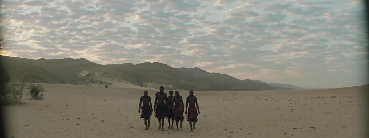 Men walking with sticks with a mountain range the sky and clouds in the background