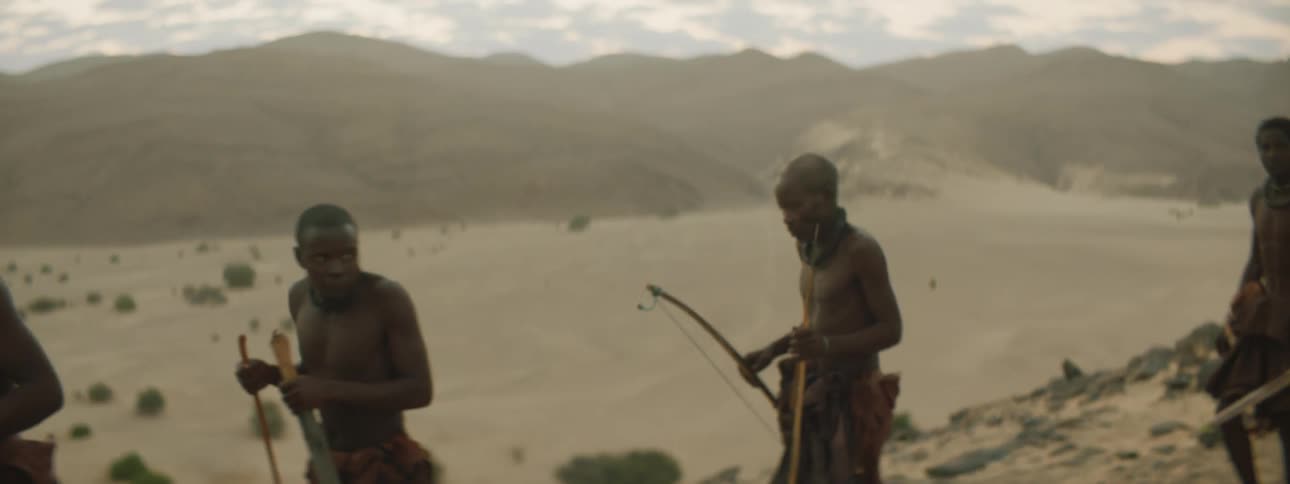 Men walking with sticks with a mountain range the sky and clouds in the background