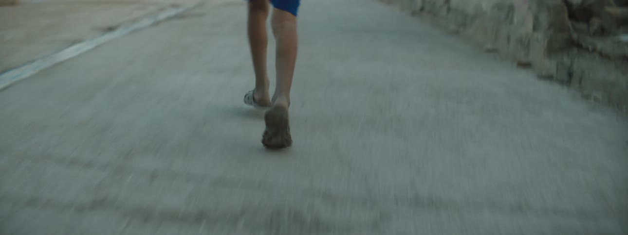 A boy runs down the road past pedestrians and ruined buildings