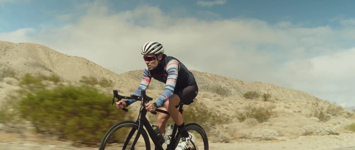 Man wearing a helmet rides a bicycle on a road in the desert close to the mountains