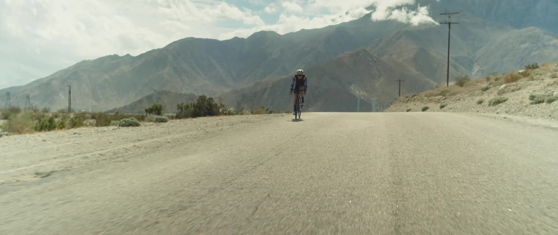 Male cyclist rides bicycle on country road with high mountains in the background