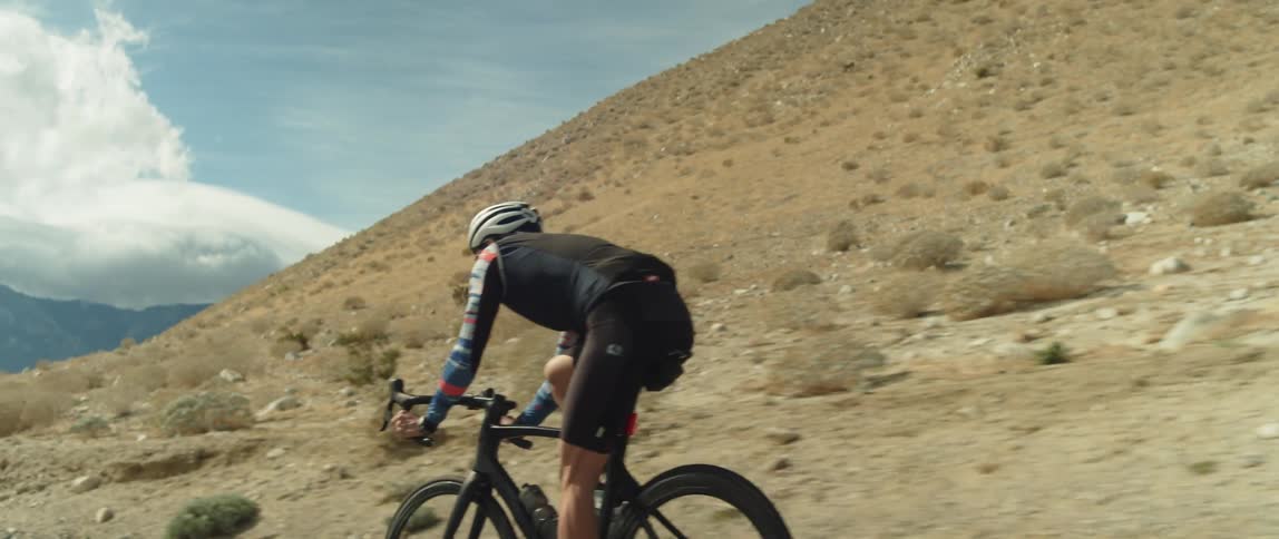 Man wearing a helmet rides a bicycle on a road in the desert close to the mountains