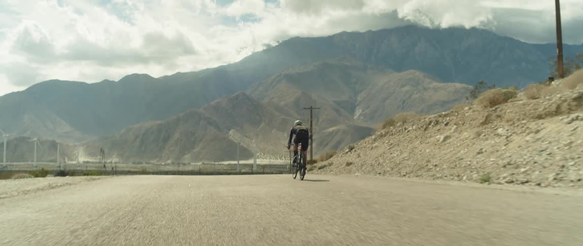 A cyclist rides along a road through a dry countryside during the day