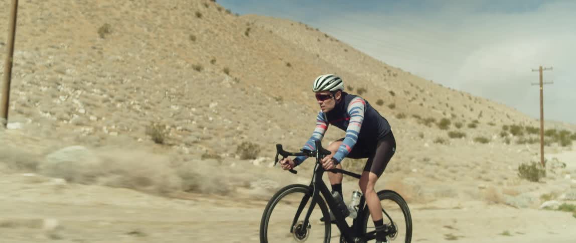 A cyclist rides a bicycle along a road through an arid countryside during the day