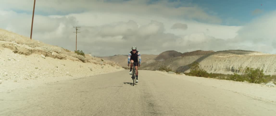 Man wearing a helmet rides a bicycle on a road in the desert close to the mountains