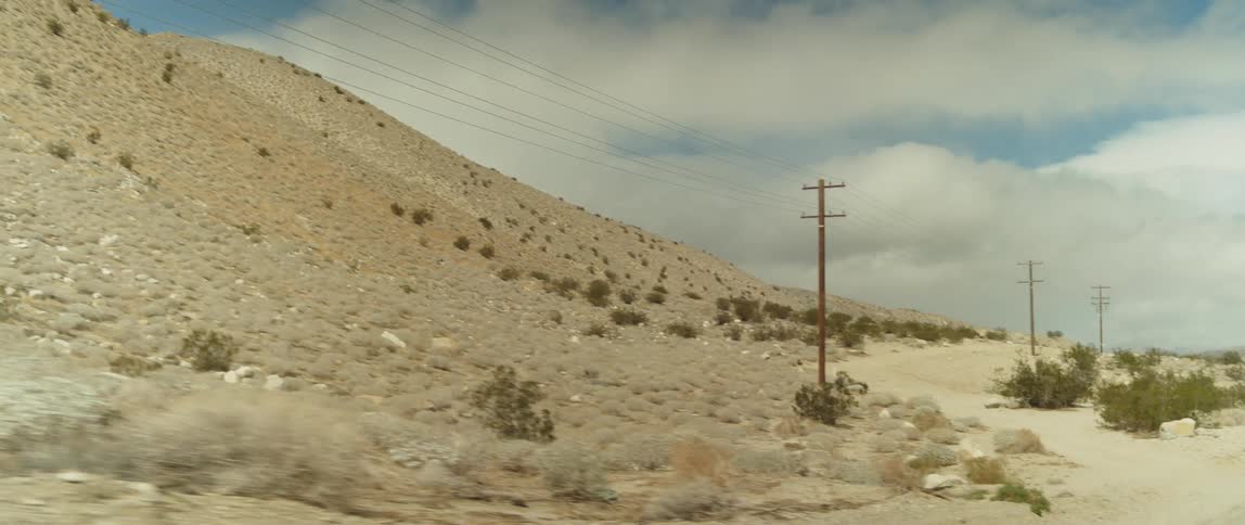 A road runs along the bottom of a large hill in an arid countryside during the day