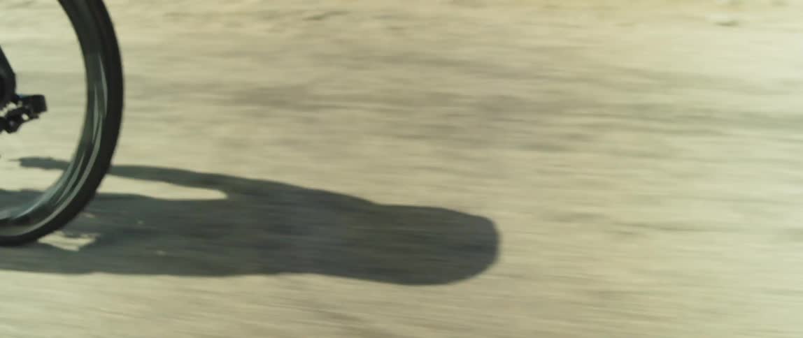 Cyclist rides along road past scrub