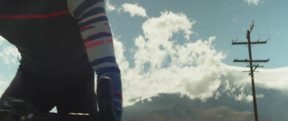 A man wearing a helmet and sunglasses is riding a bike under a cloudy sky