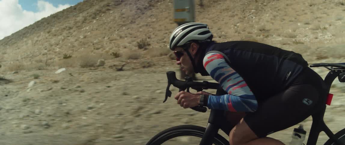 Man wearing a helmet rides a bicycle on a road in the desert close to the mountains