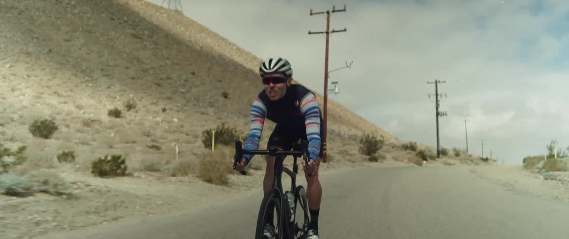 Man riding a bicycle on a road through the desert stands over the seat and changes position