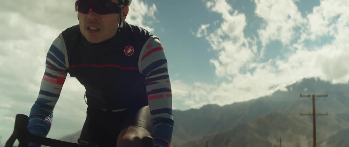 A man wearing a helmet is riding a bike and there are mountains behind him