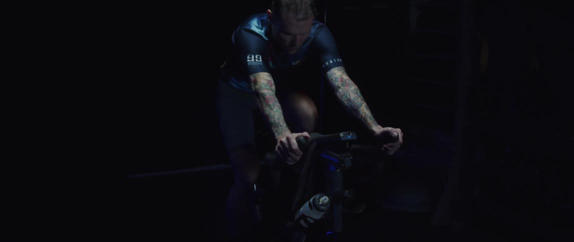 A tattooed man is riding a stationary bicycle indoors