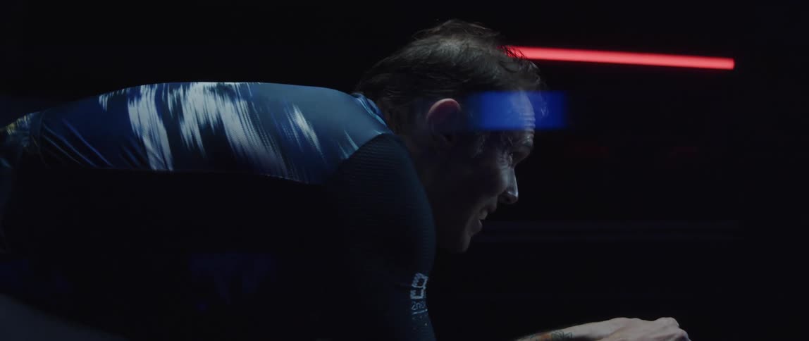 A man breathing heavily while riding a stationary bike in a dark room
