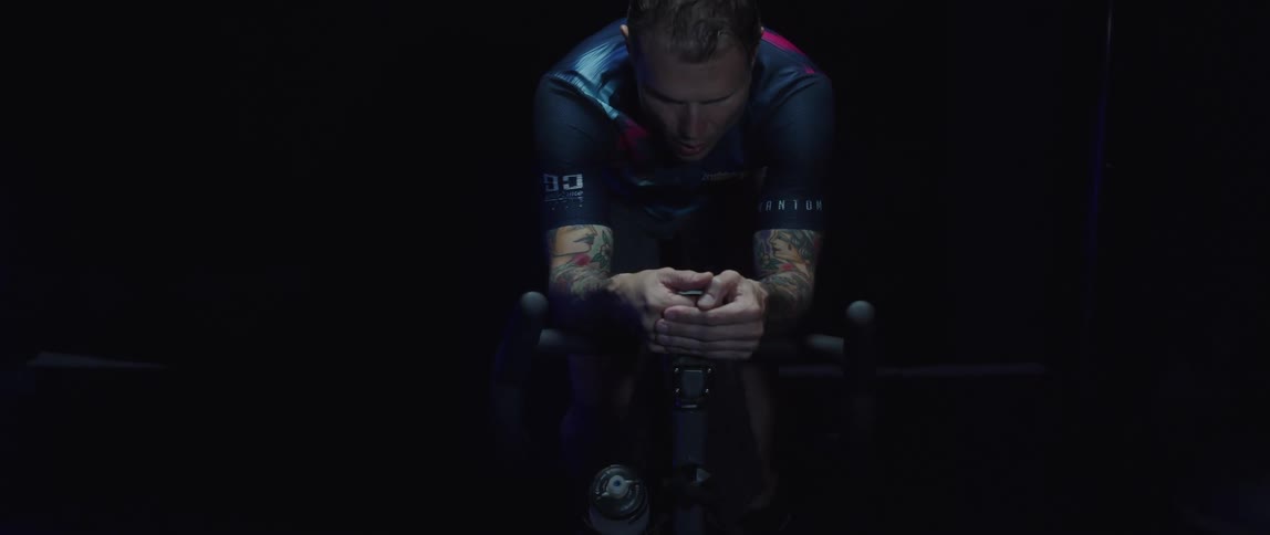 Sweaty tired man pedals on stationary bike in the dark