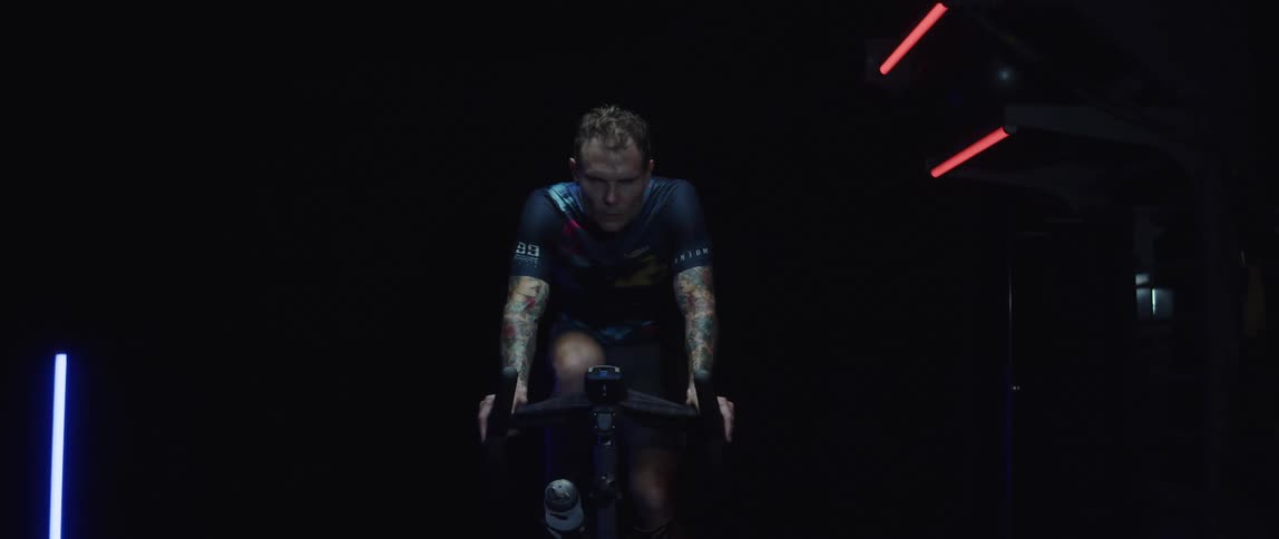 Male cyclist with jersey shirt and tattoos rides exercise bike
