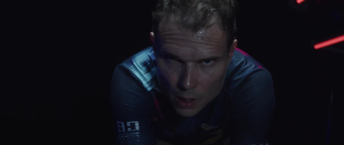 Determined male cyclist with jersey shirt and tattoos rides exercise bike