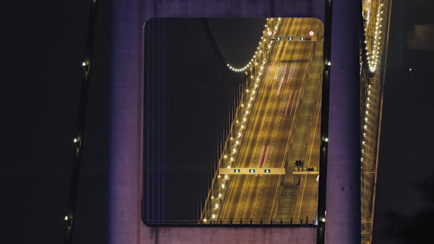 Heavy traffic drives down a suspension bridge at night