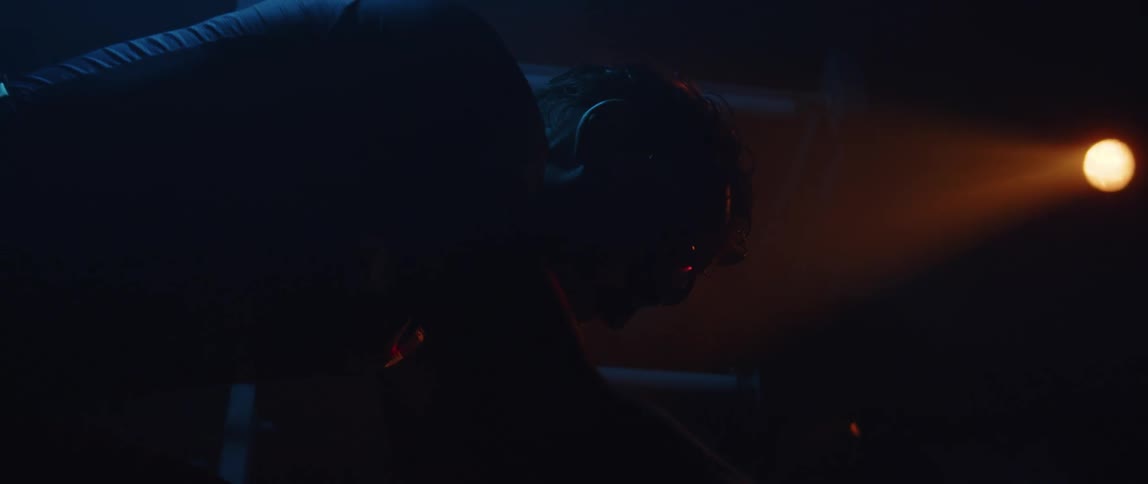 Silhouette of a man pedaling on a static bicycle inside a dimly lit room under a spotlight
