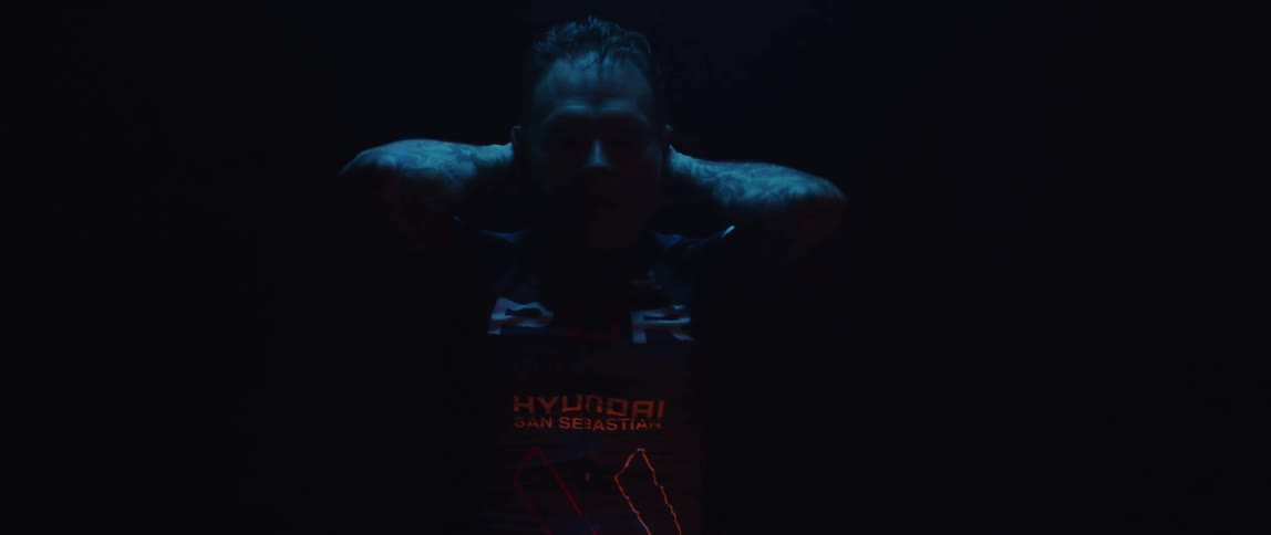 Man pedaling on a static bicycle inside a dimly lit room against a dark background