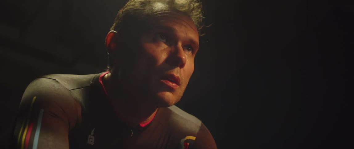Man pedaling on a static bicycle inside a dimly lit room against a dark background