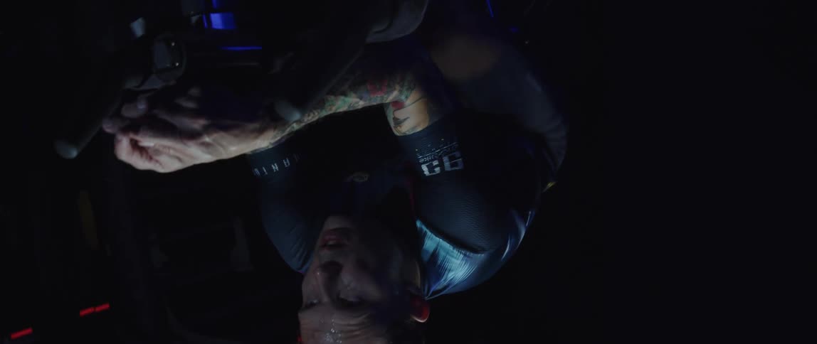 Twisting footage of a man pedaling on a static bicycle inside a dimly lit room against a dark background