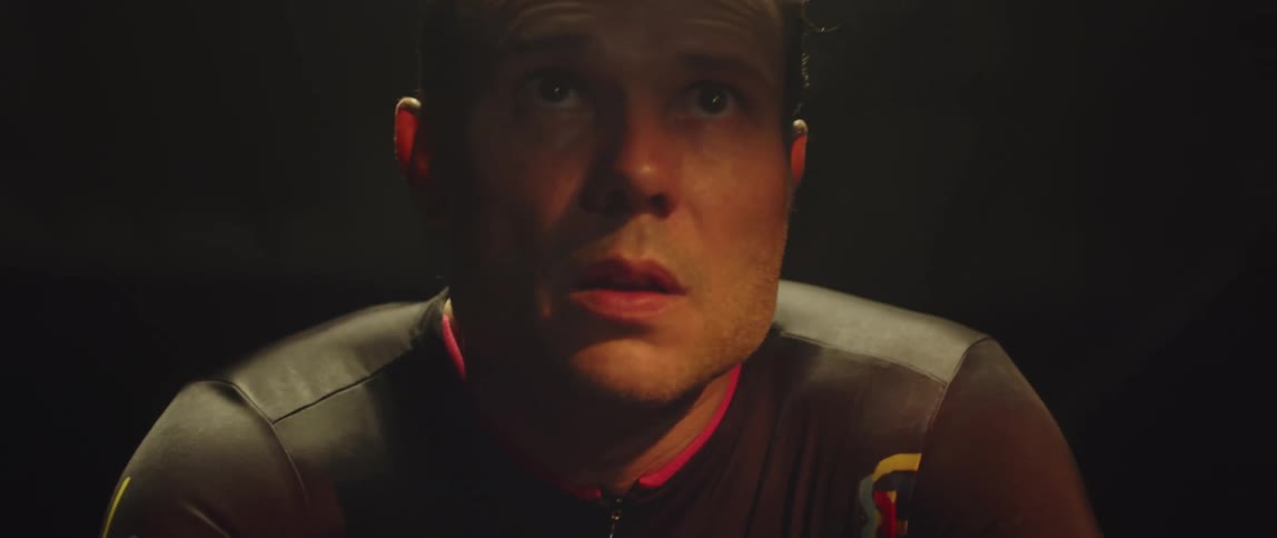 Close up of the face of a man pedaling a static bicycle inside a dimly lit room