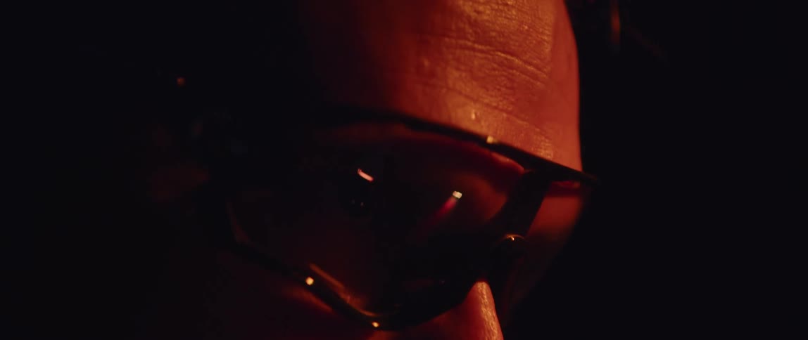 Close up of the face of a man wearing sunglasses inside a dimly lit room