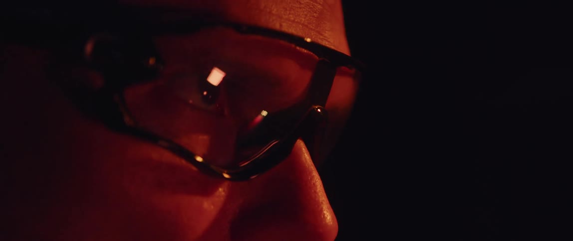 Close up of the face of a man pedaling a static bicycle inside a dimly lit room