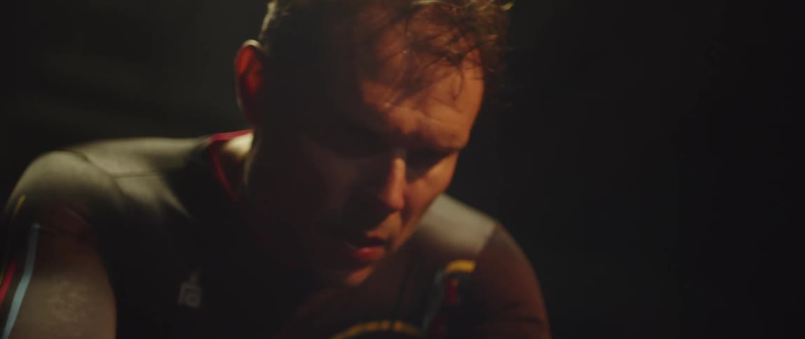 Male cyclist with jersey shirt rides exercise bike in dark room