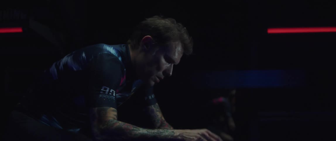 A man changes his posture while using an exercise bike in a dark room