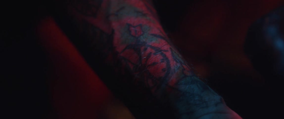 Tattoo on the forearm of a man riding a static bicycle glowing under red lights