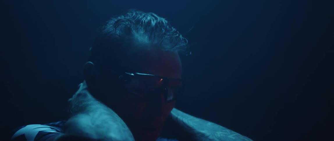 Man breathes deeply and rests his hands on the back of his neck in a dark room