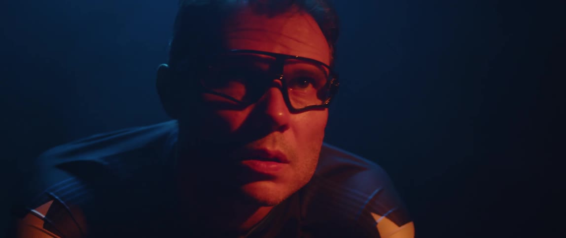 Close up of the face of a man pedaling a static bicycle inside a dimly lit room