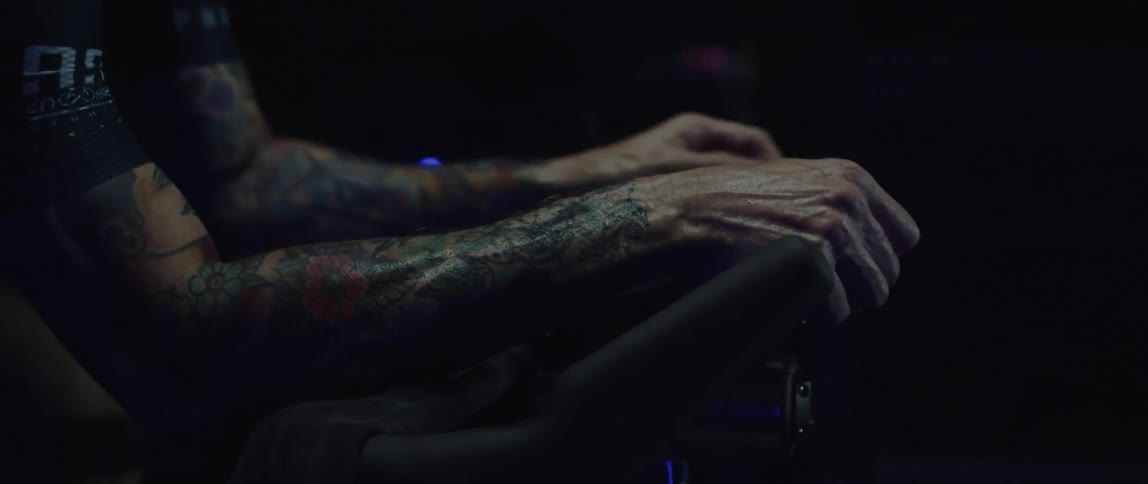 Cyclist man exercising on a stationary bike in a dark room with his hands on the handlebar