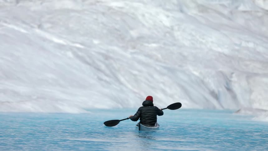 A kayaker paddles on icy blue waters near a glacier