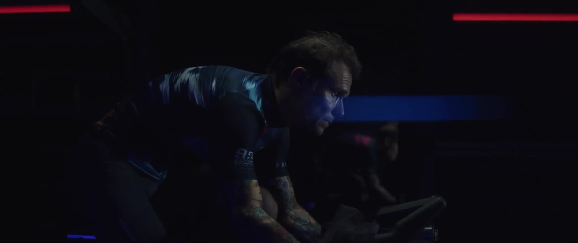 Male cyclist with jersey shirt and tattoos rides exercise bike