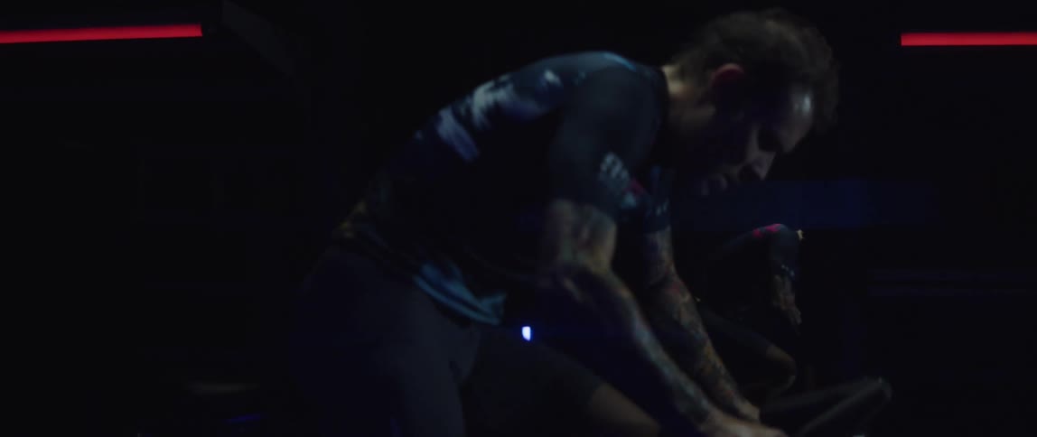 A man stands while pedaling an exercise bike in a dark room