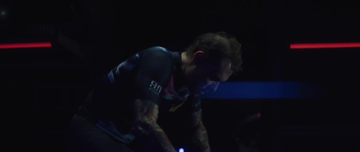 Focused man wearing a cycling jersey exercising on a stationary bike in a dark gym room