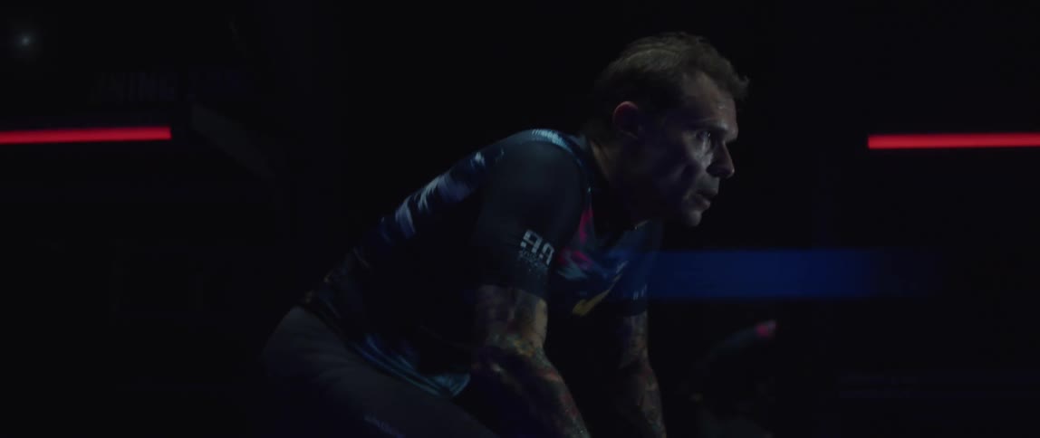 A tattooed man sweating while working out on a stationary bike